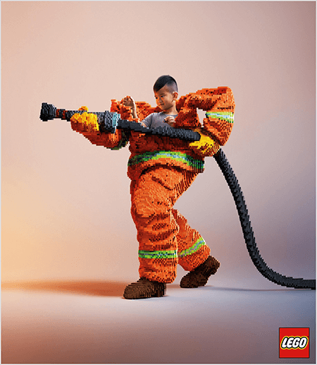 Dette er et bilde fra en LEGO-annonse som viser en ung asiatisk gutt inne i en brannmannuniform laget av LEGO. Uniformen er oransje med en neongrønn stripe rundt ermene på kåpen og buksene. Brannmannen står med en fot bak og holder en brannslange, også laget av legoer. Guttens hode vises ut av toppen av uniformen, som er mye større enn han er og stopper rundt skuldrene. Bildet er tatt mot en ren nøytral bakgrunn. LEGO-logoen vises i en rød boks nederst til høyre. Talia Wolf sier LEGO er et godt eksempel på et merke som bruker følelser i reklame.